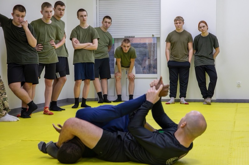 An instructor demonstrates a hold as a group of students look on.