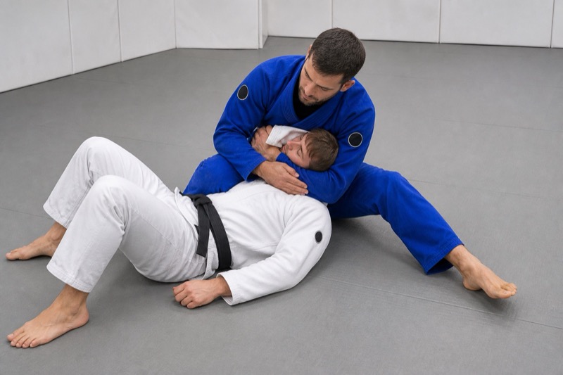 The top player sits beside the opponent, wrapping the head in the scarf hold kesa-gatame.