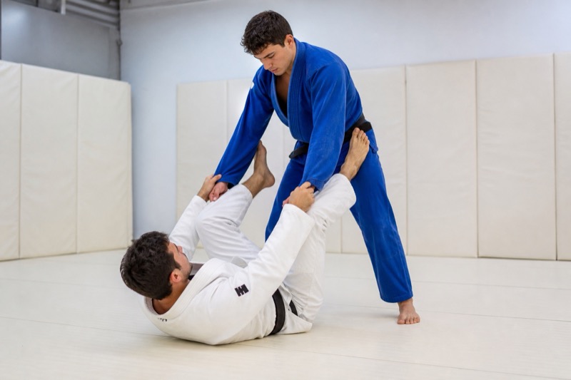 A guard player on their back plants both feet on a standing opponent's hips in open guard.