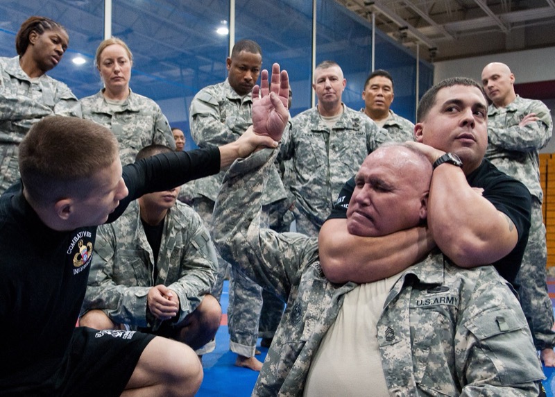 An instructor demonstrates a rear naked choke on a training partner while others watch.